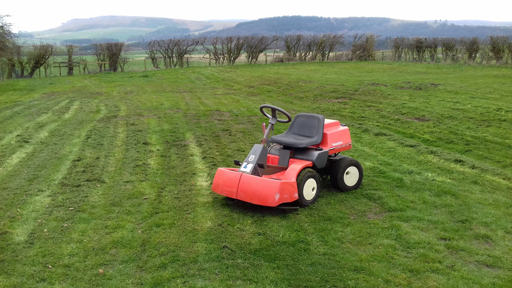 A ride-on mower on a freshly striped field with hills behind